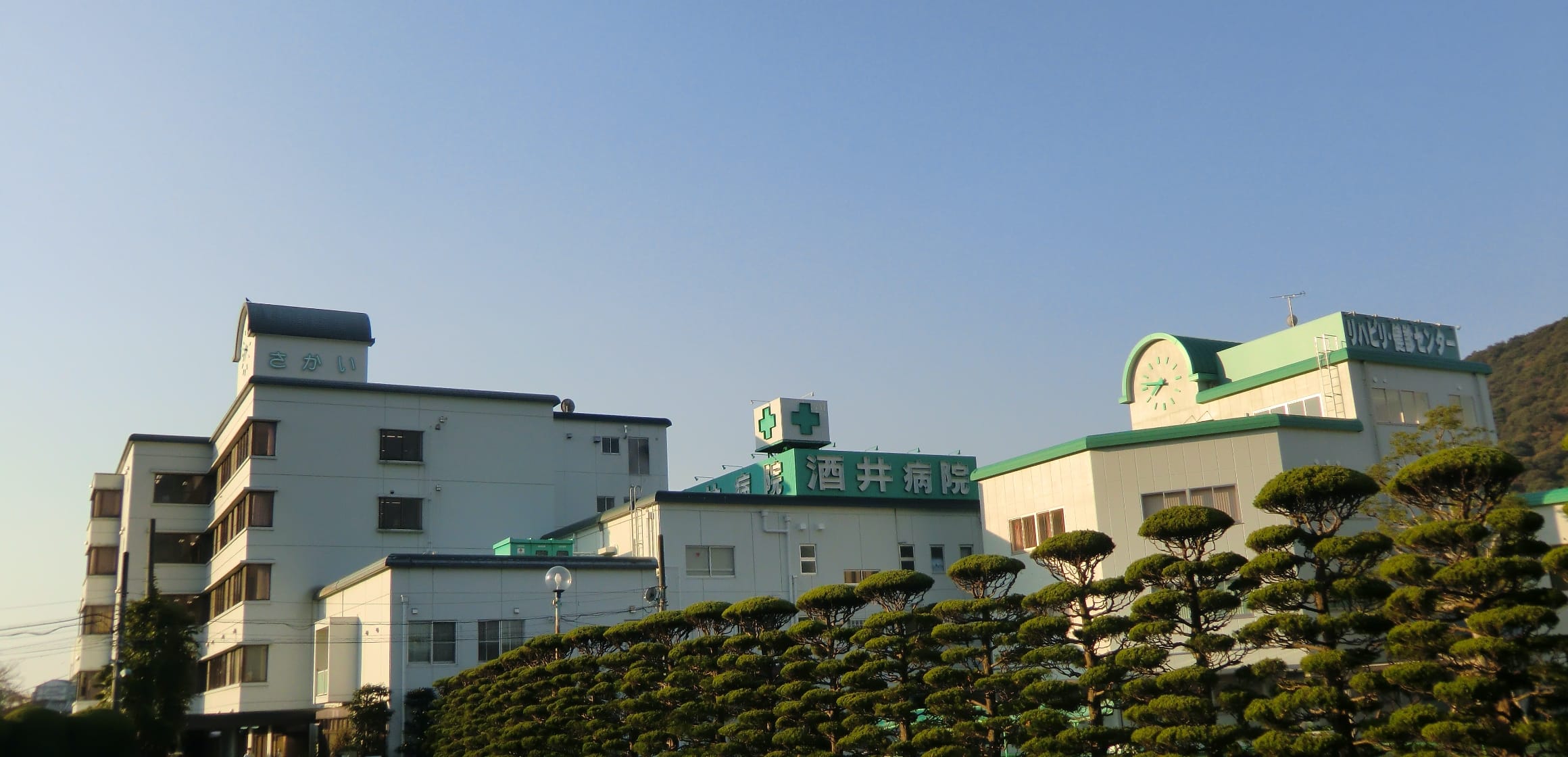 介護施設の建物外観。複数棟の白い建物と緑色の看板が見える。